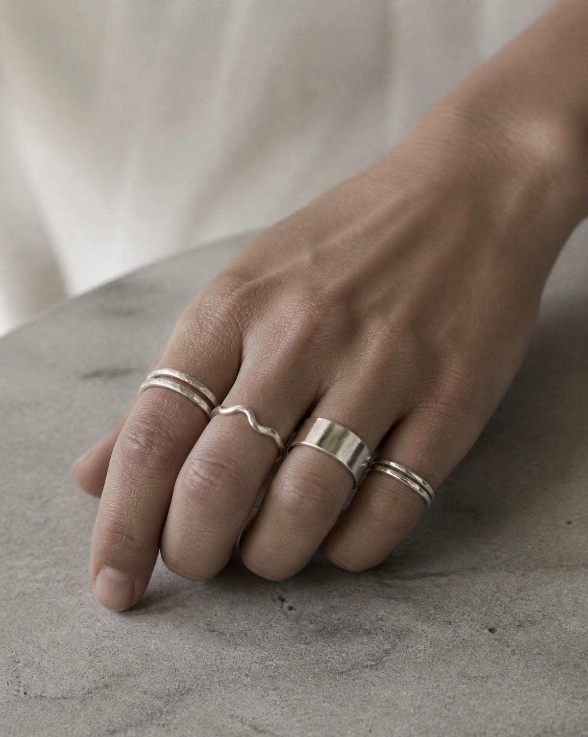 Mano con anillos de plata contemporáneos sobre superficie de piedra